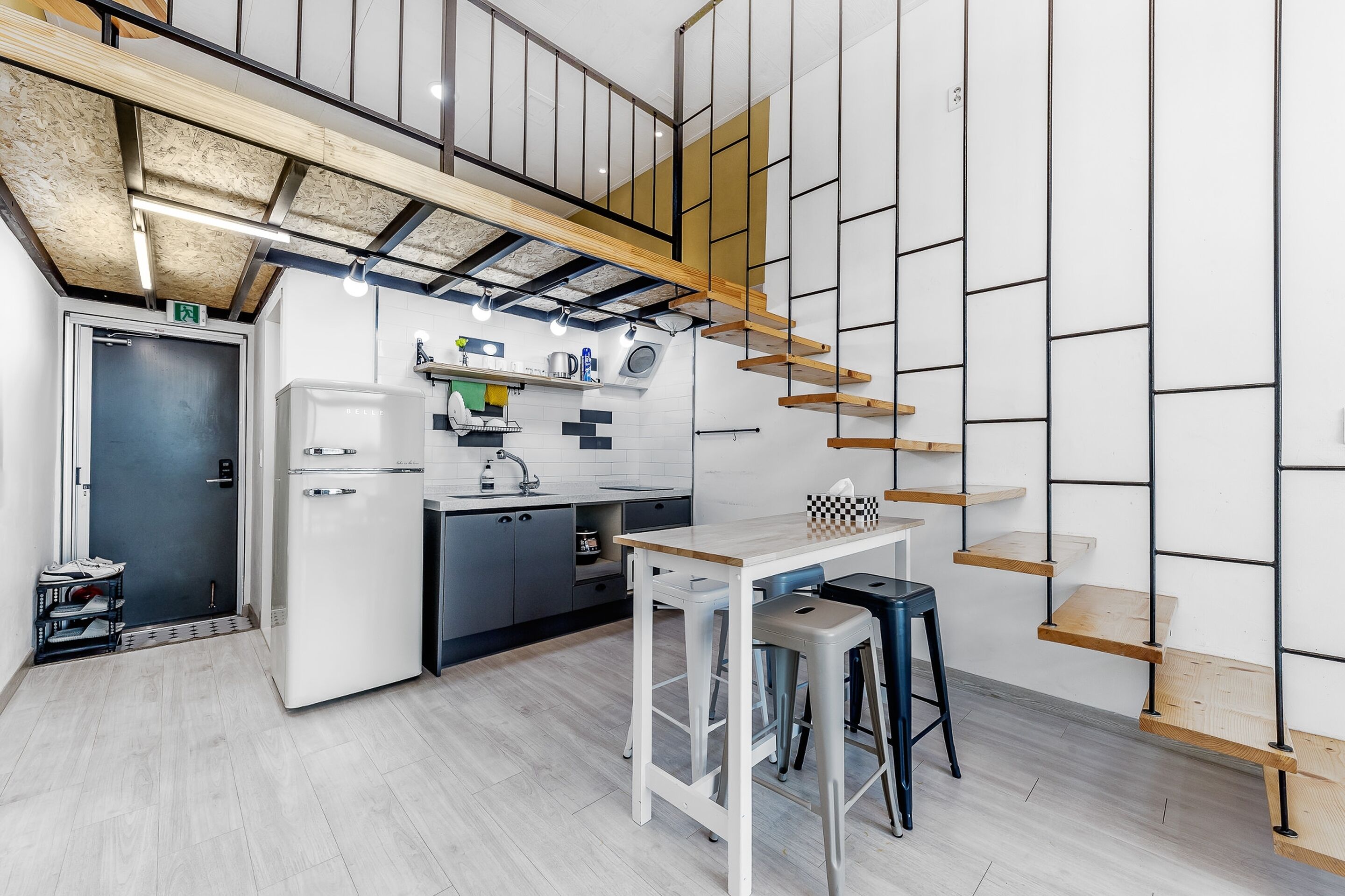 A modern kitchen with a built-in refrigerator, a coffee machine, and a wooden staircase.
