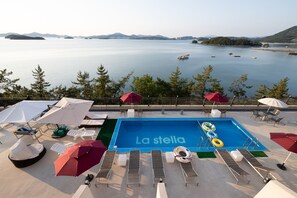 A rooftop pool with 'La stella' written on the water, surrounded by lounge chairs and umbrellas, overlooking a calm sea with boats. - Yeosu Lastella Spa Pet-friendly Pension (Yeosu)