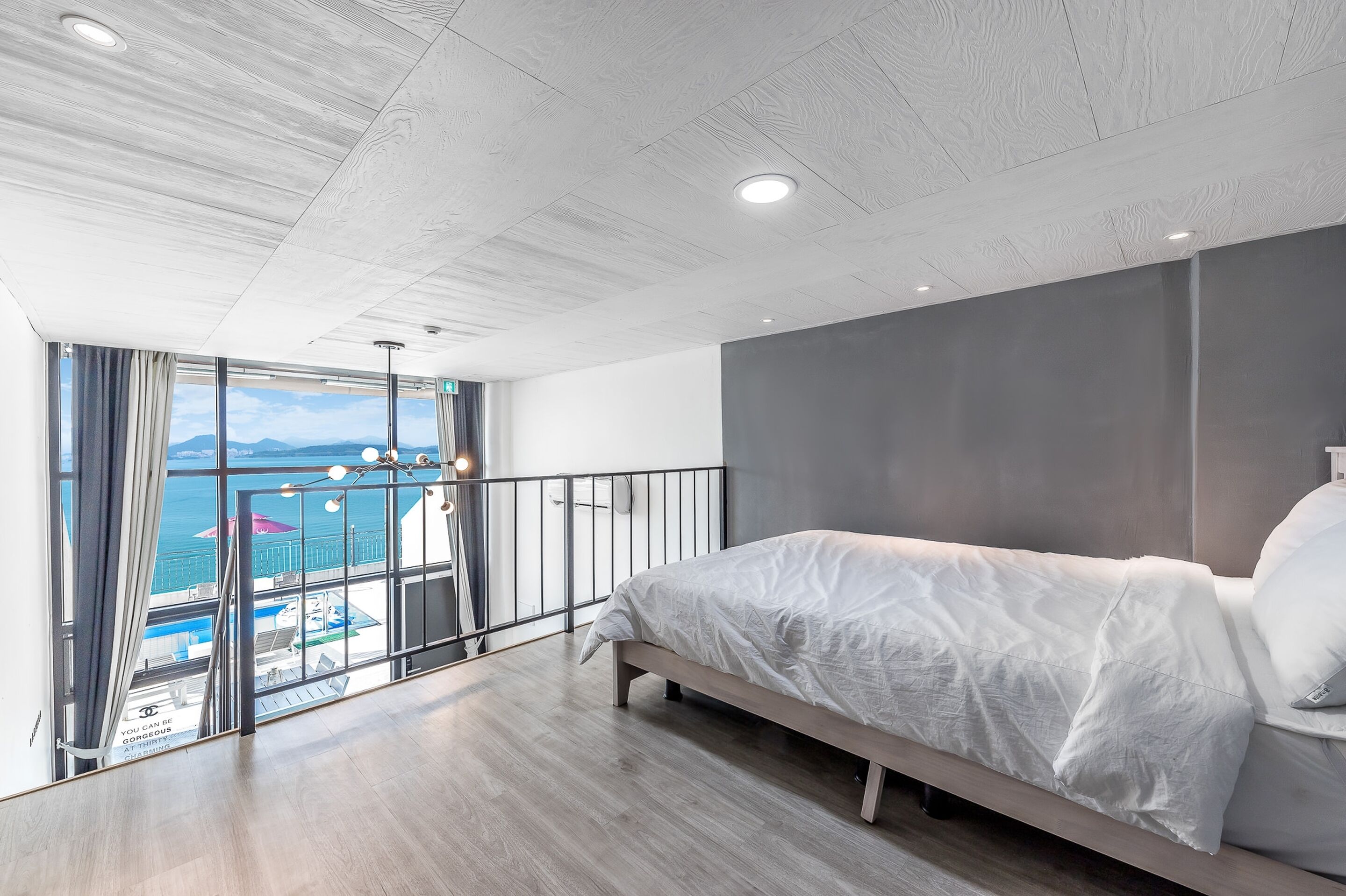 Un dormitorio moderno con una cama grande, un balcón con vistas al mar y techo de madera.