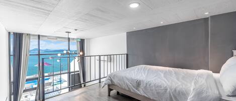 Un dormitorio moderno con una cama grande, un balcón con vistas al mar y techo de madera.
