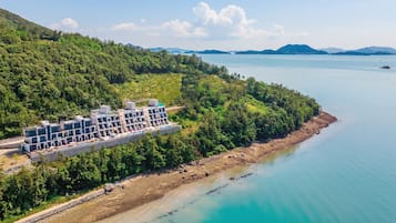 A coastal hotel with multiple buildings, a beach, and a forested hillside.