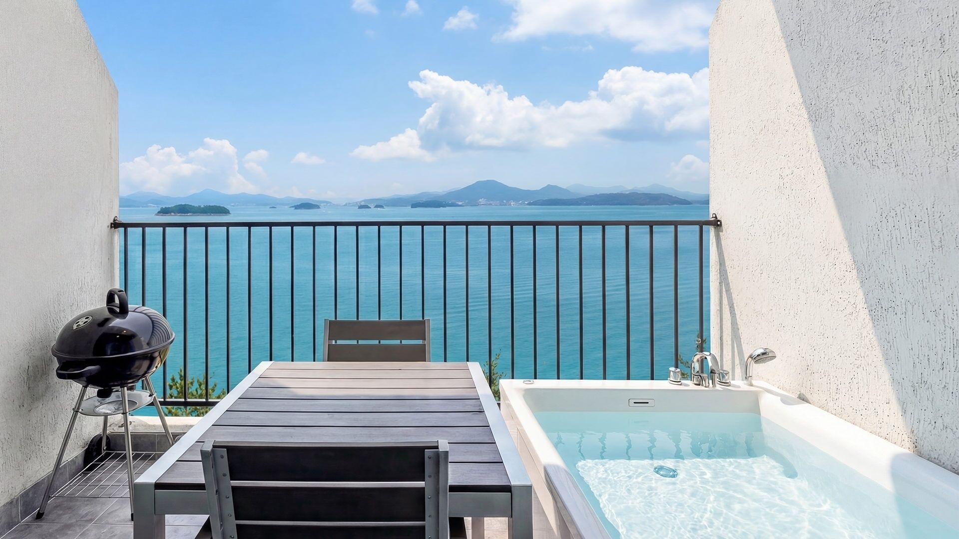 Un balcón con vista al mar, una parrilla, una mesa y un jacuzzi.