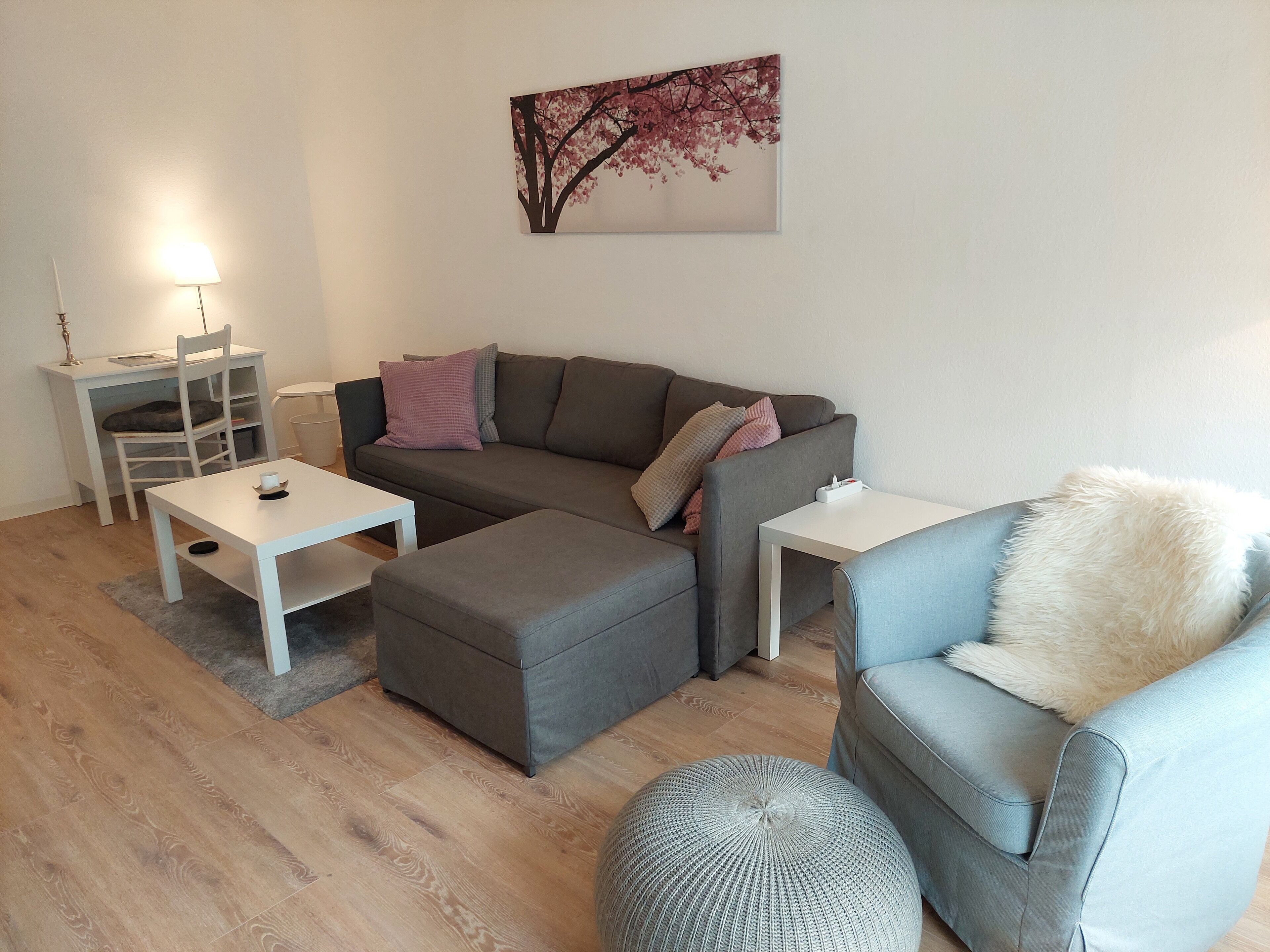 A modern living room with a grey sofa, a small table, a chair, and a round ottoman.