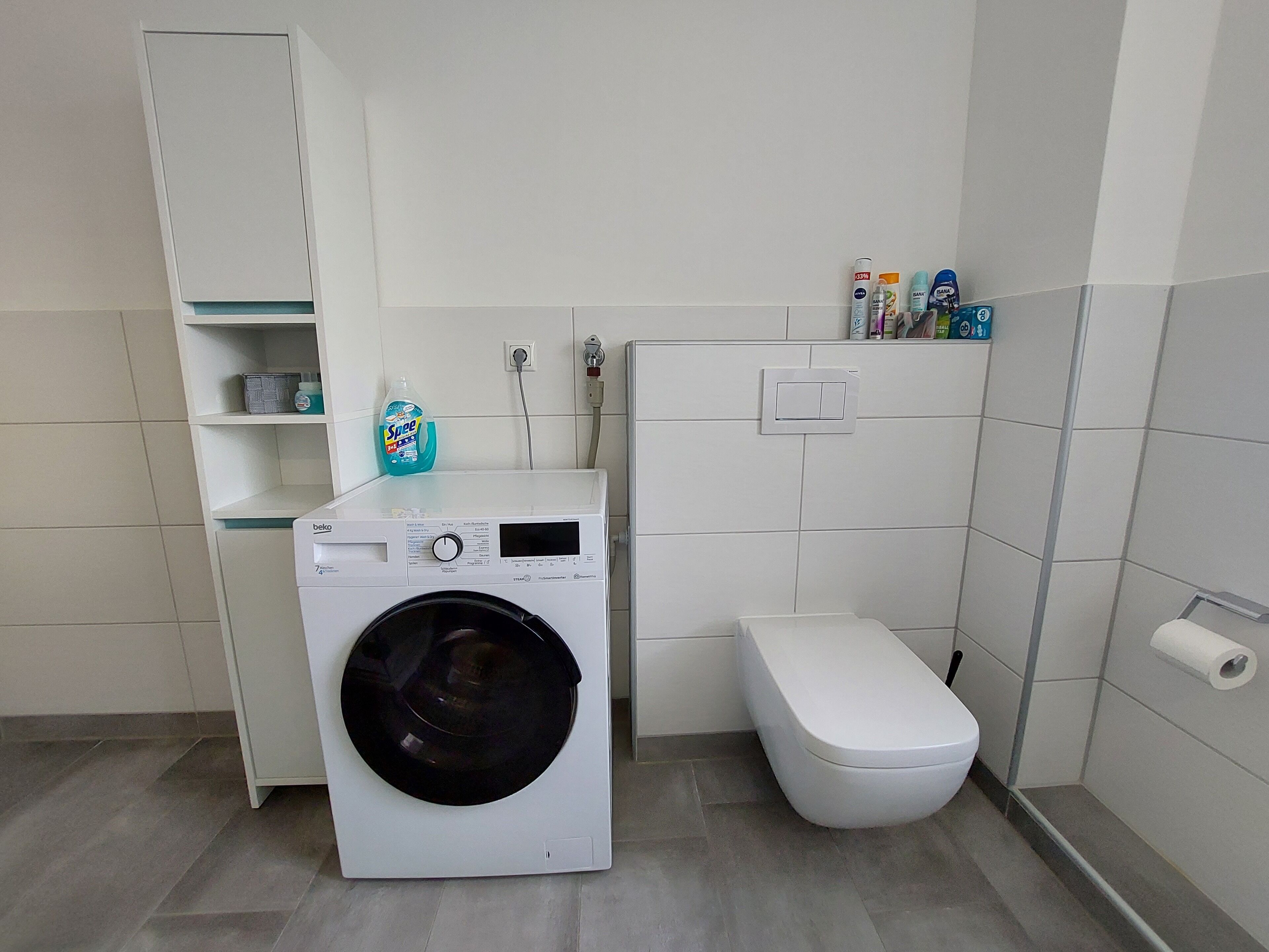 Ein kleines Badezimmer mit Waschmaschine, Toilette und Regalen mit Pflegeprodukten.