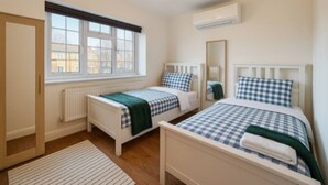 Ein Schlafzimmer mit zwei Einzelbetten, einem Fenster mit Jalousien, einem Heizkörper und einem Spiegel an der Wand.