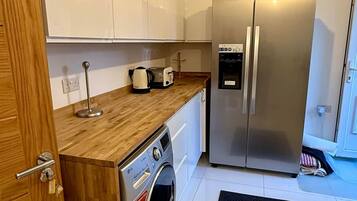 A compact kitchen with a stainless steel refrigerator, a built-in washing machine, and a wooden countertop.