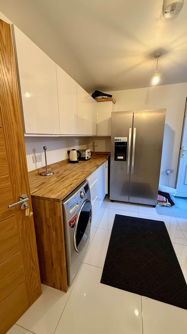 Una cocina compacta con refrigerador de acero inoxidable, lavadora integrada y encimera de madera.