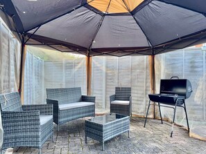 A covered outdoor seating area with wicker furniture and a grill. - 5 Bedroom Home in Central London| Air conditioned! (London)
