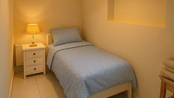 A bedroom with a bed, bedside table, lamp, and a chair.