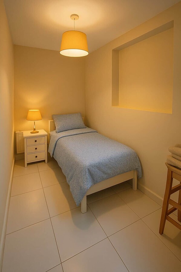 A bedroom with a bed, bedside table, lamp, and a chair.