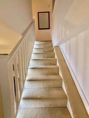 A carpeted staircase with white railings, leading to a landing with a framed picture. - 5 Bedroom Home in Central London| Air conditioned! (London)