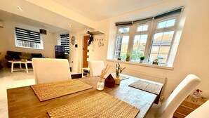 Ein Essbereich mit einem Holztisch, zwei gewebten Tischsets, weißen Stühlen und einem Fenster mit Jalousien.