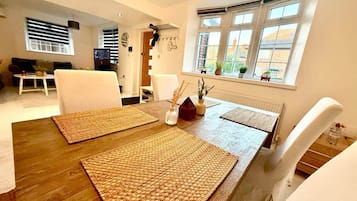 A dining area with a wooden table, woven placemats, white chairs, and a window with blinds.