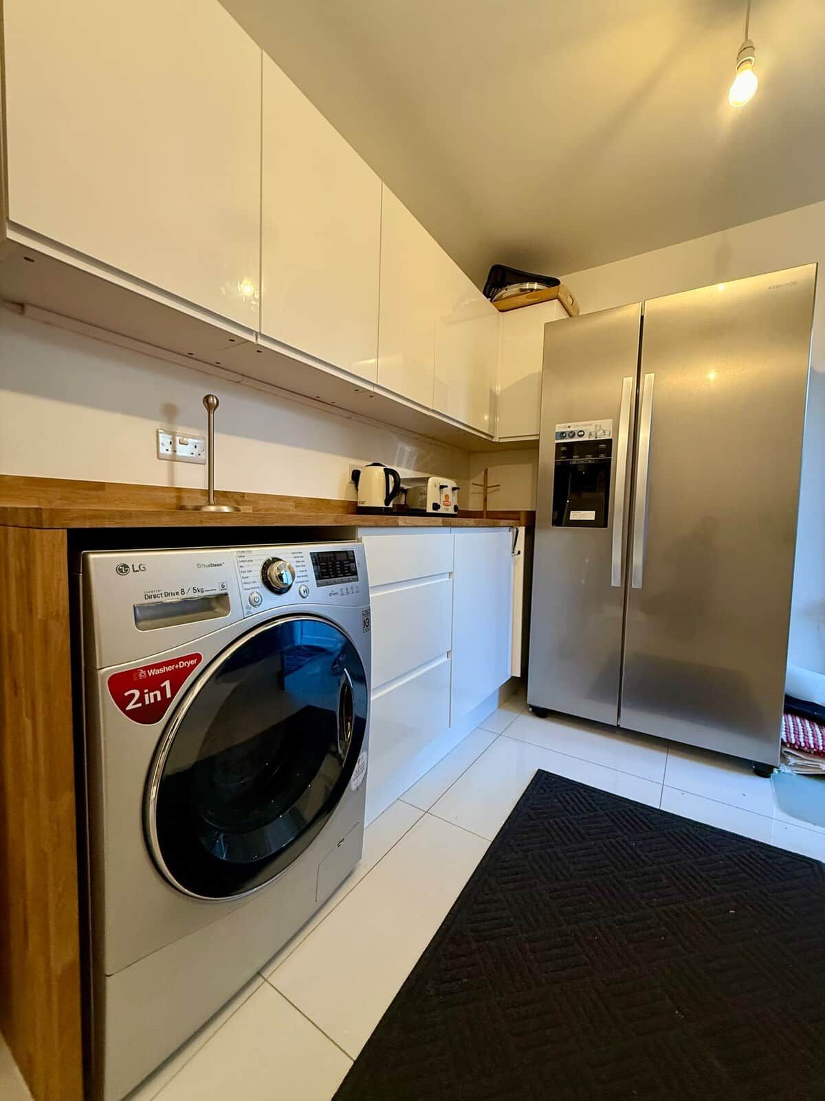 A compact kitchen with a washing machine, a refrigerator, and a coffee maker.