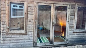 Eine rustikale Holzhütte mit einem großen Schiebeglastür, einem kleinen Fenster und einem sichtbaren Innenraum mit einem Bett und einem Tisch.
