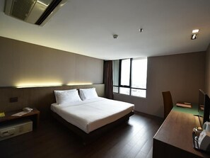 Une chambre d’hôtel moderne dotée d’un grand lit, d’un bureau et d’une fenêtre laissant entrer la lumière naturelle.