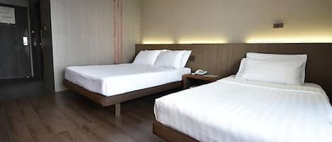 A hotel room with two single beds, a wooden floor, a wall-mounted phone, and a door leading to another room.