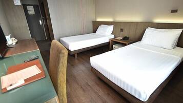 Ett hotellrum med två separata sängar, ett skrivbord med en stol och ett litet bord med en telefon och papper.