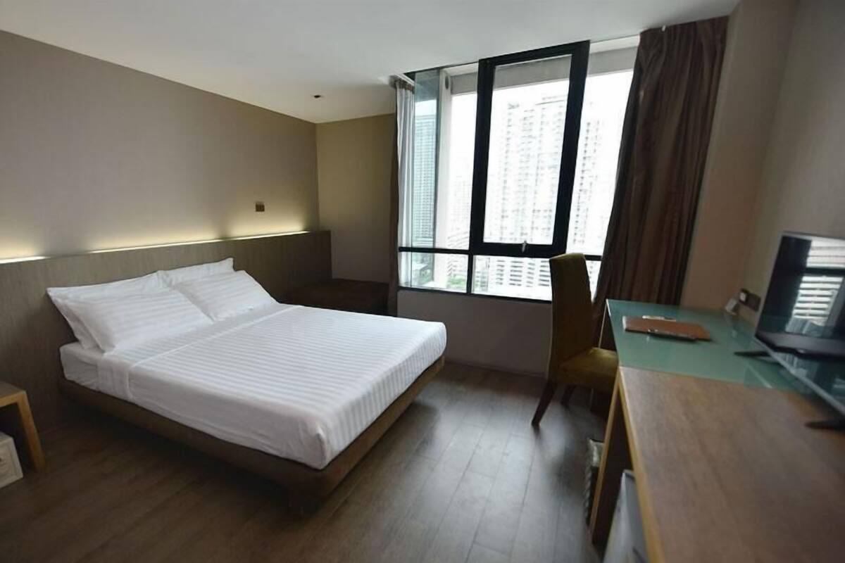 Hotelkamer met een bed, bureau, stoel, televisie en raam met gordijnen.