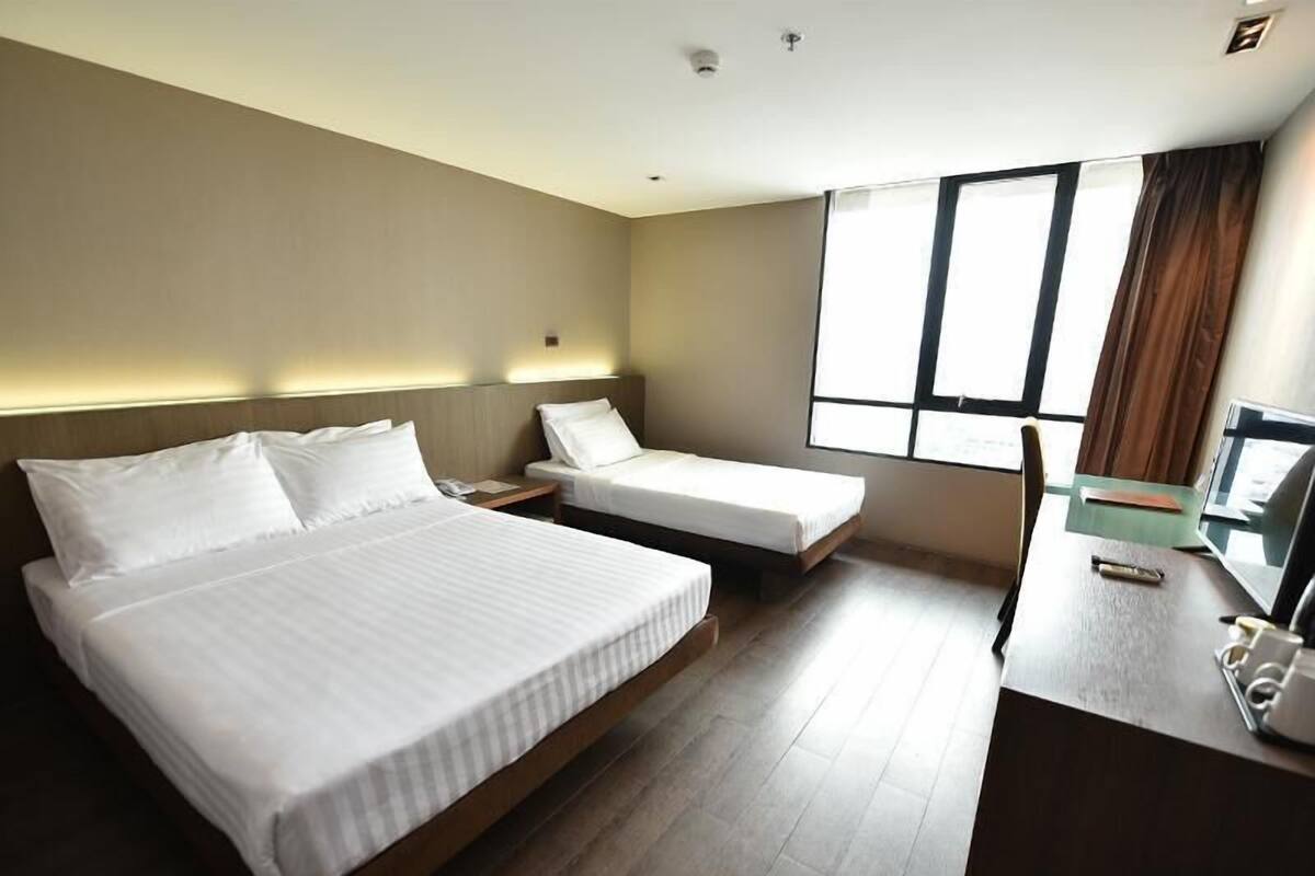 Een hotelkamer met twee eenpersoonsbedden, een bureau met een computer en een groot raam met gordijnen.