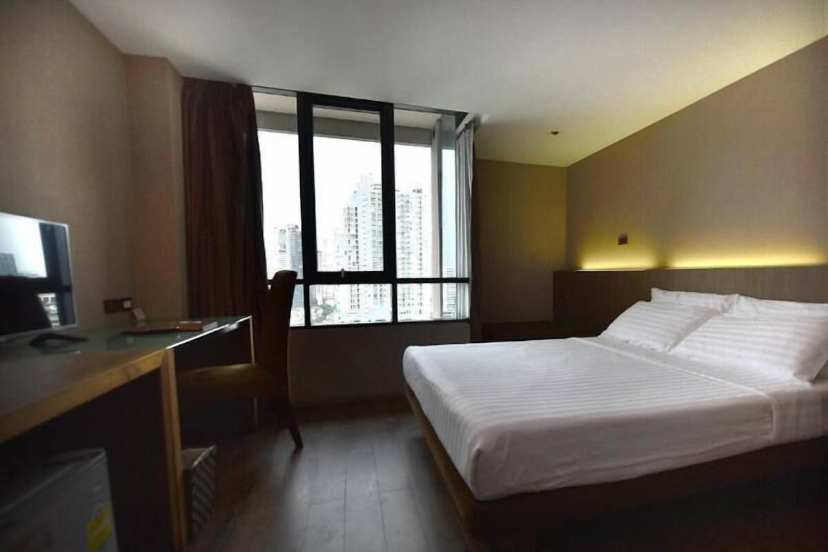 Een hotelkamer met een bed, een bureau, een stoel en een groot raam met uitzicht op de stad.