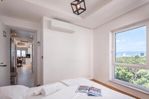A modern bedroom with a large window, a bed, and a view of the city. - Seaview Apartment Kostrena Two (Kostrena)