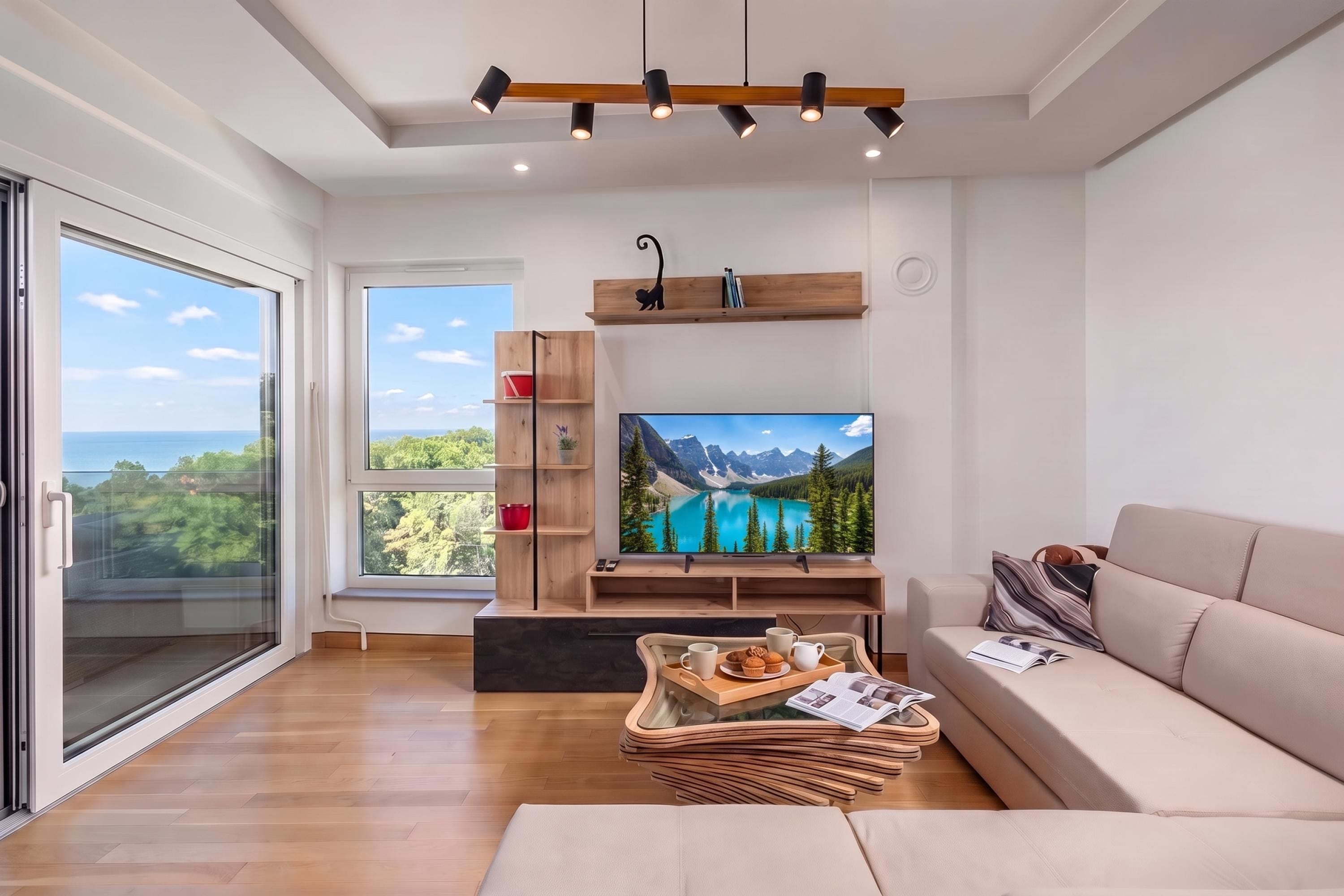 A modern living room with a large TV, wooden shelving, and a view of the outdoors.