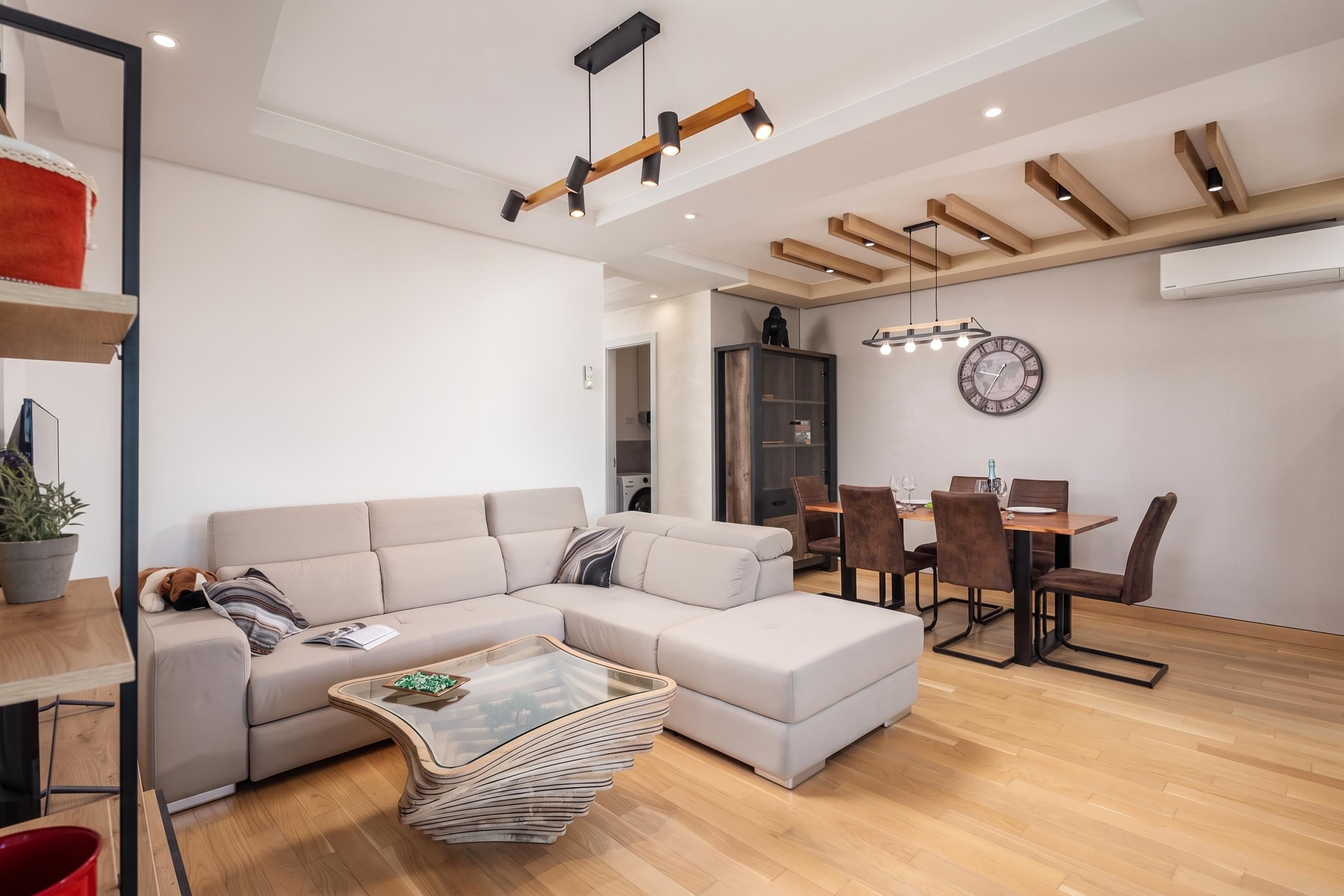 A modern living room with a sectional sofa, a glass coffee table, and a dining area with a wooden table and chairs.