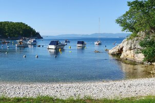 A calm harbor with boats anchored in clear water, surrounded by rocky shores and greenery.