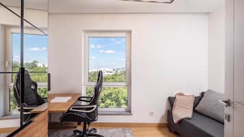 A modern room with a desk, two chairs, a sofa, and a large window offering a city view.