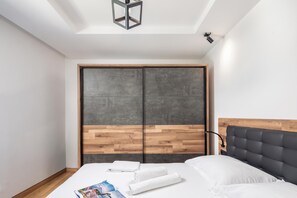 A modern bedroom with a bed, a wooden headboard, a wardrobe with a concrete panel, and a skylight. - Seaview Apartment Kostrena Two (Kostrena)