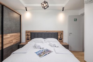 Moderni hotellihuone, jossa on puinen sängynpääty, suuri sänky valkoisilla vuodevaatteilla, kaksi yöpöytää ja lehti sängyllä.