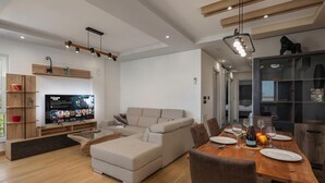 A modern living room with a sofa, dining table, and TV. - Seaview Apartment Kostrena Two (Kostrena)