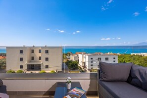 A balcony with a sofa and a table, overlooking a coastal view with buildings and the sea. - Seaview Apartment Kostrena Two (Kostrena)