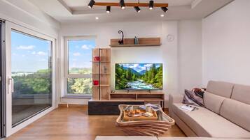 A modern living room with a large flat-screen TV, wooden shelves, a sofa, and a dining area with a tray of food.
