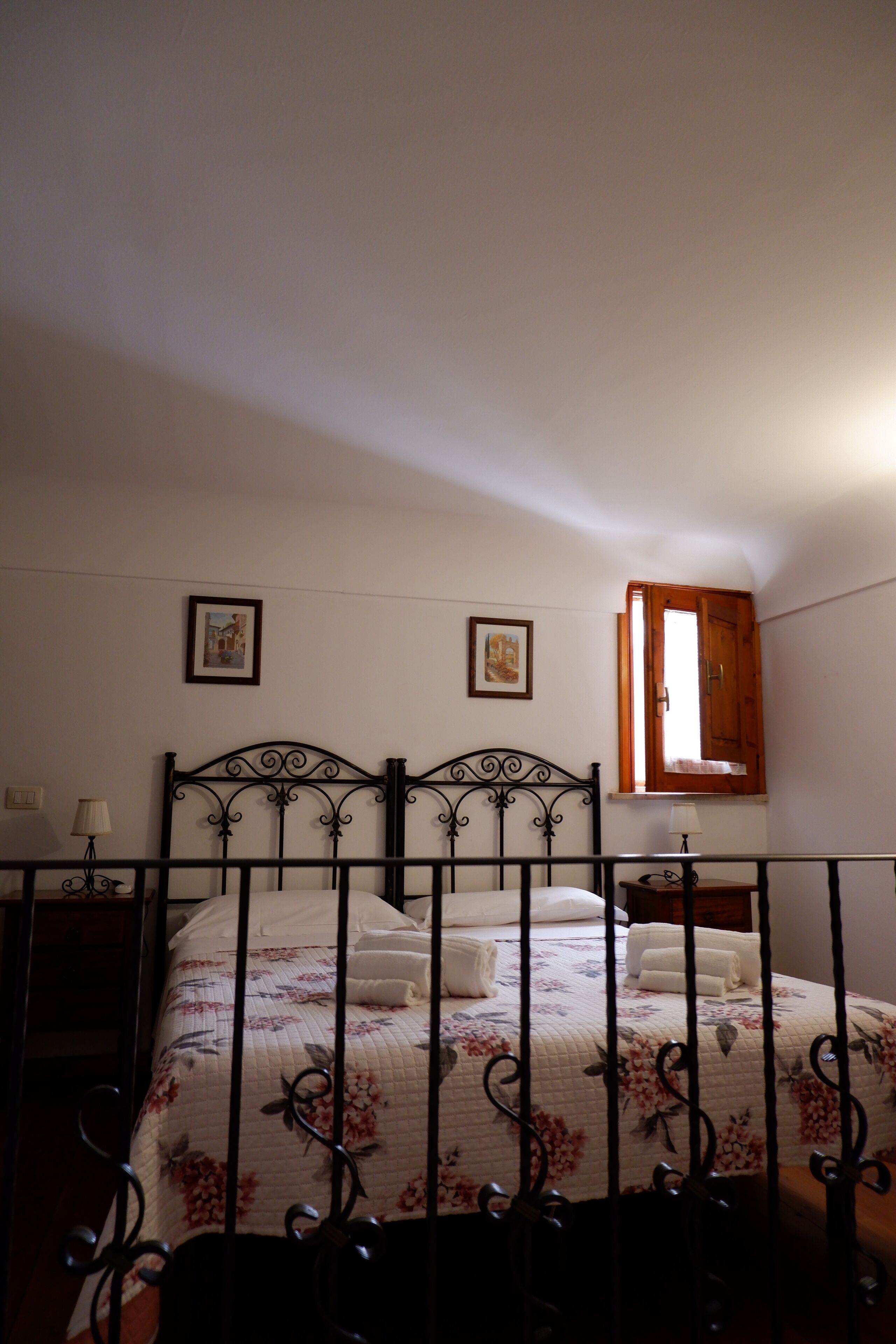 A bedroom with a bed, two wall-mounted lamps, and a window with a wooden door.
