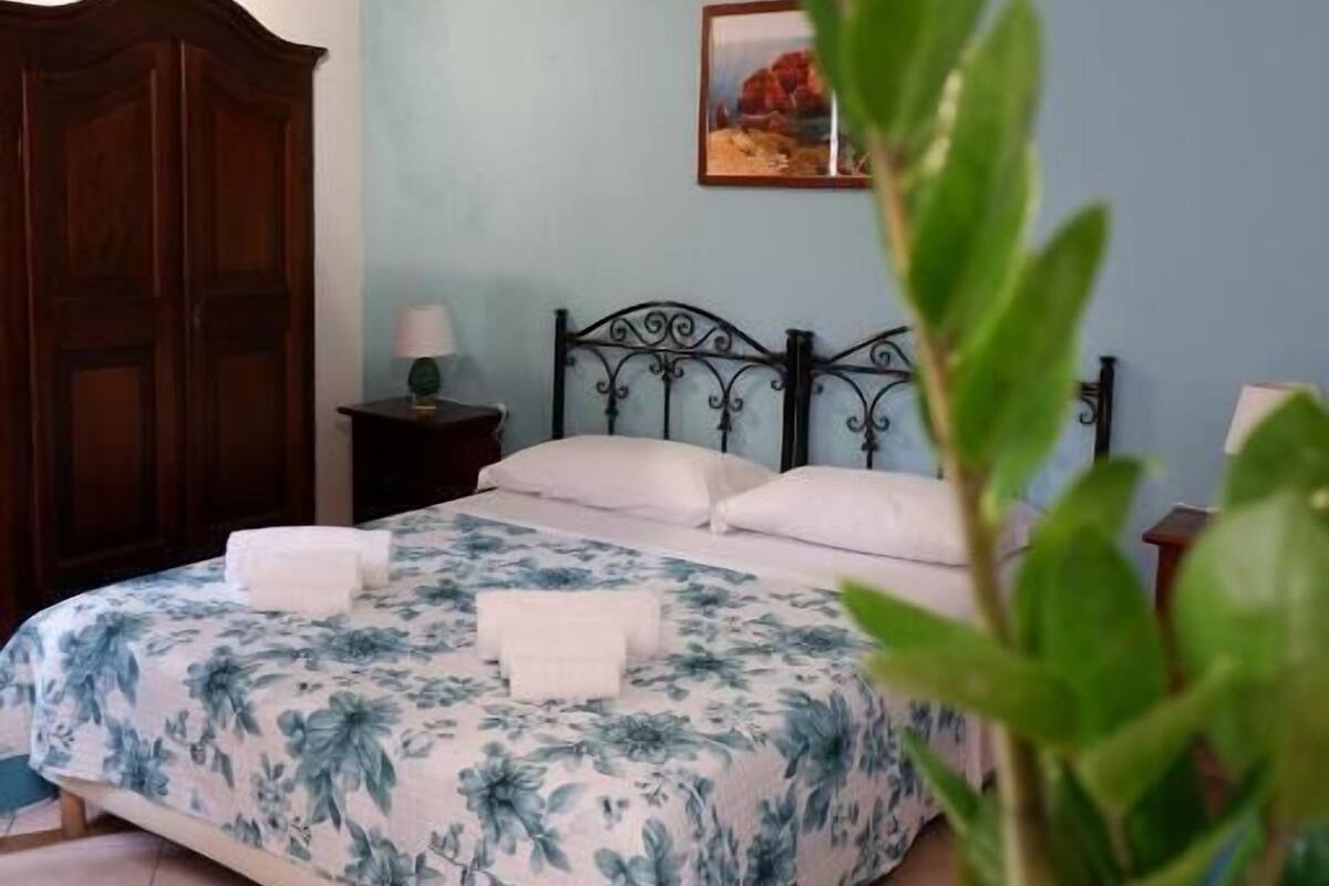Ein Schlafzimmer mit einem Bett, einem Nachttisch, einer Topfpflanze und einer Klimaanlage.