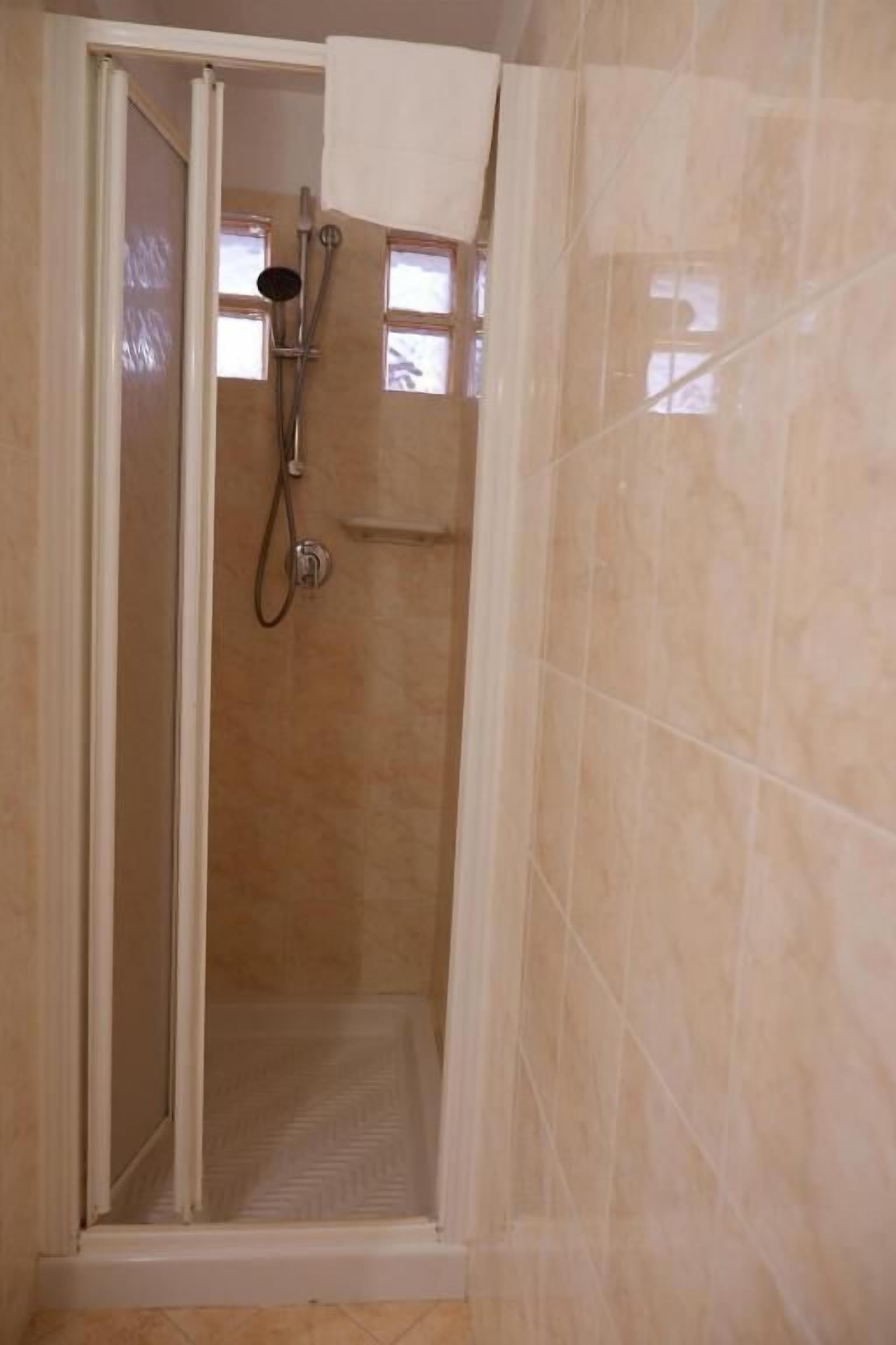 A shower with a glass door, a handheld showerhead, and a towel hanging on the wall.