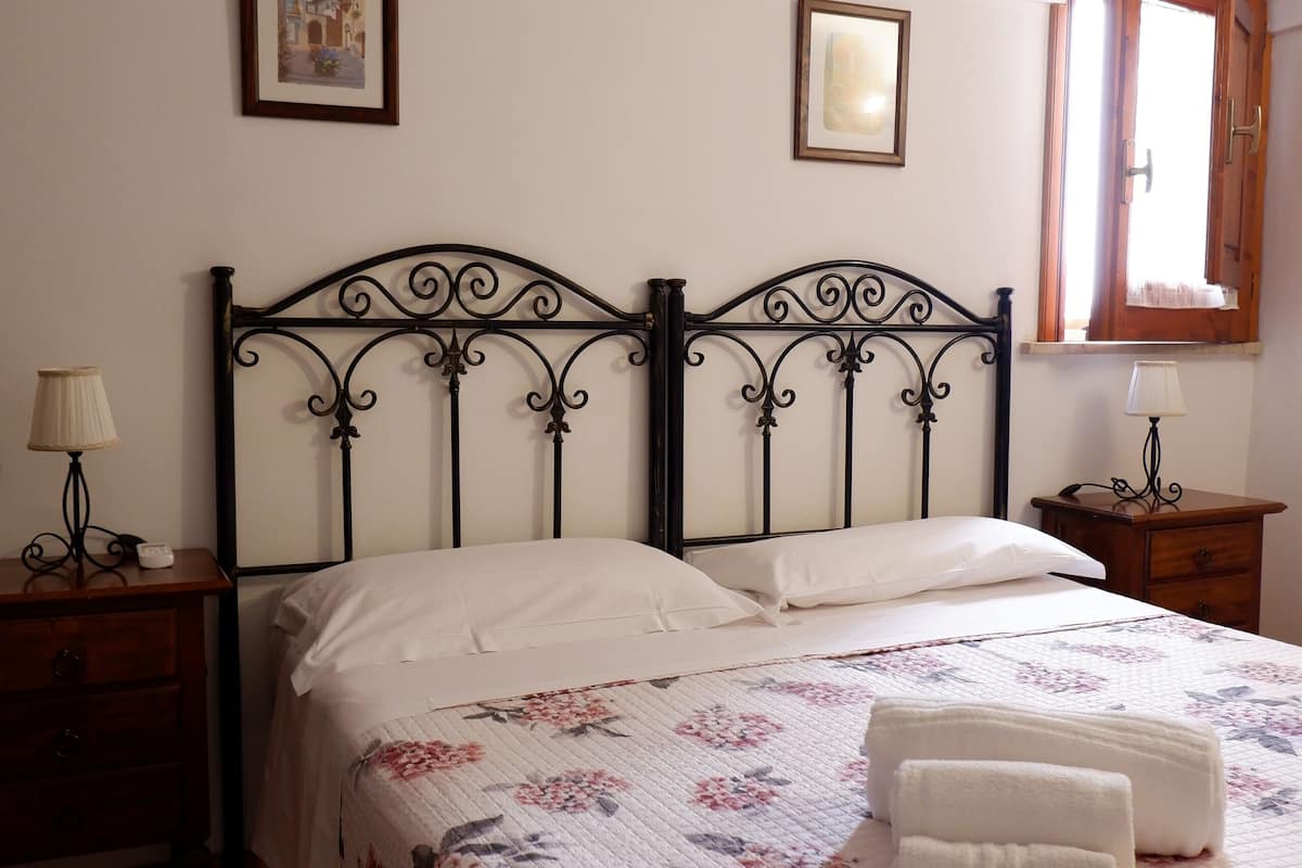 Ein Schlafzimmer mit Bett, Nachttisch, Kommode, einem Fenster mit Vorh ängen und zwei gerahmten Bildern an der Wand.
