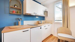 A compact kitchen with white cabinets, a built-in microwave, and a window with curtains.