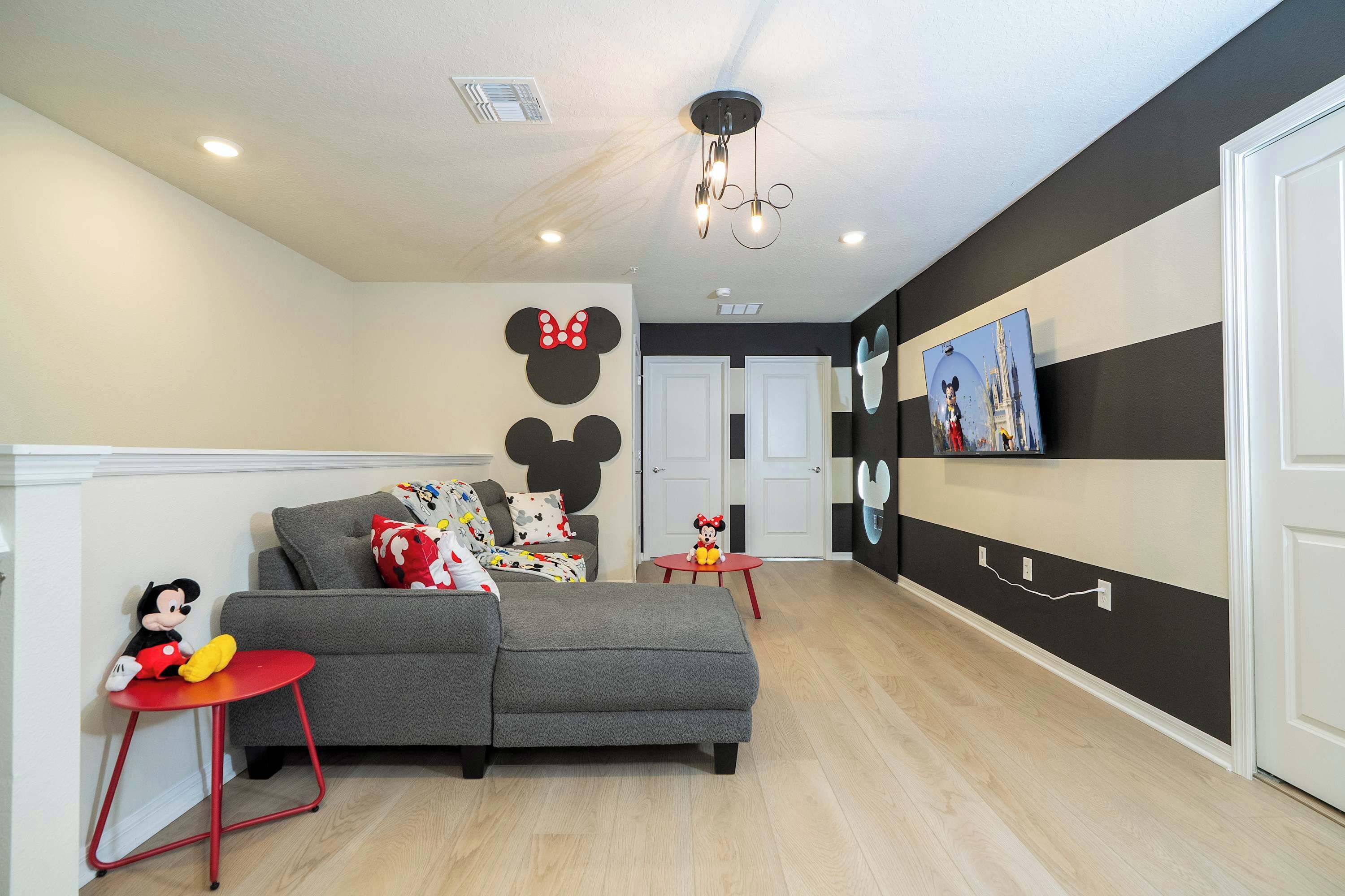 Una sala moderna con un sofá seccional gris, una mesa roja y decoración de pared con Mickey Mouse.