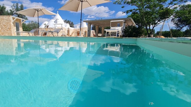 Uma piscina límpida com espreguiçadeiras e guarda-sóis, rodeada por edifícios de pedra e árvores.