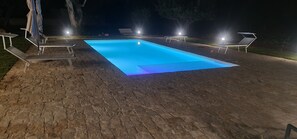 Piscina rectangular con un contorno luminoso azul, rodeada por un patio de piedra.