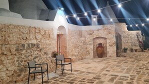 Pátio interno com paredes de pedra, uma porta de madeira e duas cadeiras.