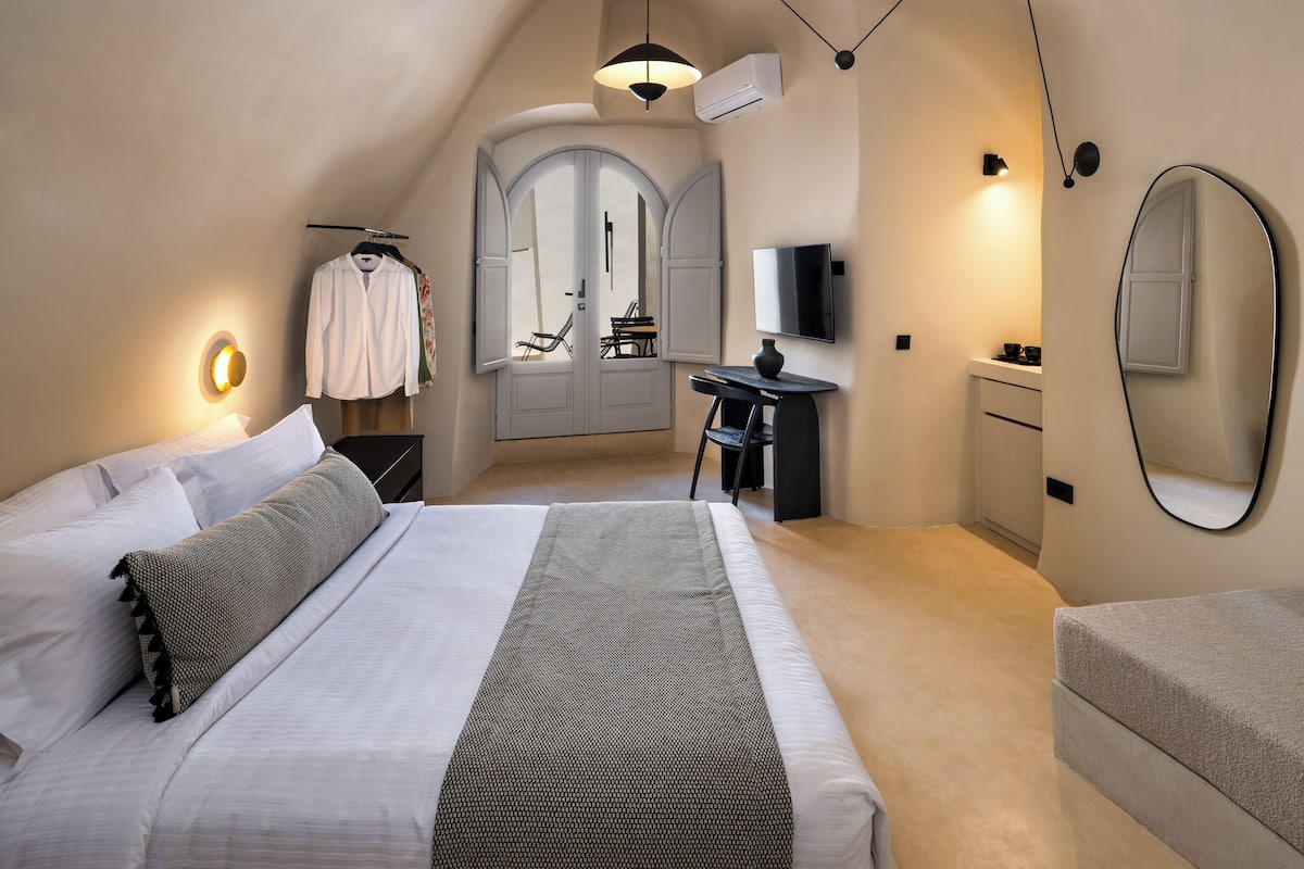 A bedroom with a bed, a desk, a chair, a TV, and a mirror.