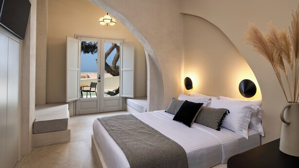 Un dormitorio con una cama grande, un área de descanso con una silla y vistas a través de una puerta abierta.