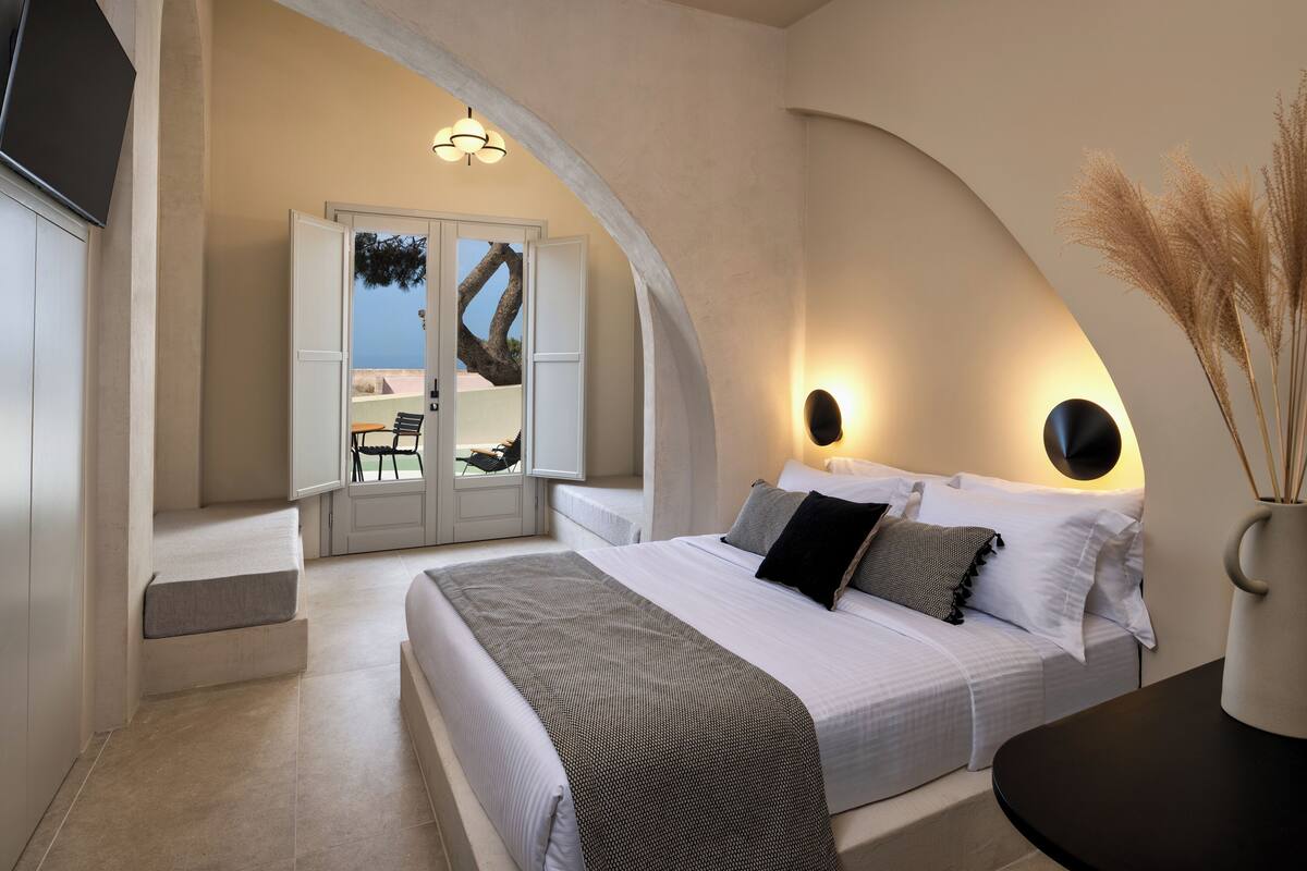 A bedroom with a large bed, a seating area with a chair, and a view through an open door.