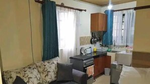 A compact room with a sofa, a bed, a kitchenette, and a window with curtains. - Mountain view Spring (Nairobi)