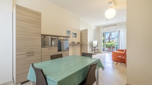Una cocina compacta con electrodomésticos modernos, una mesa de comedor con sillas y vistas al exterior a través de un ventanal grande.