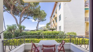 A balcony with a white table and two red chairs, overlooking a landscaped garden and a building with balconies. - Next to the Beach by Wonderful Italy (Ospedaletti)